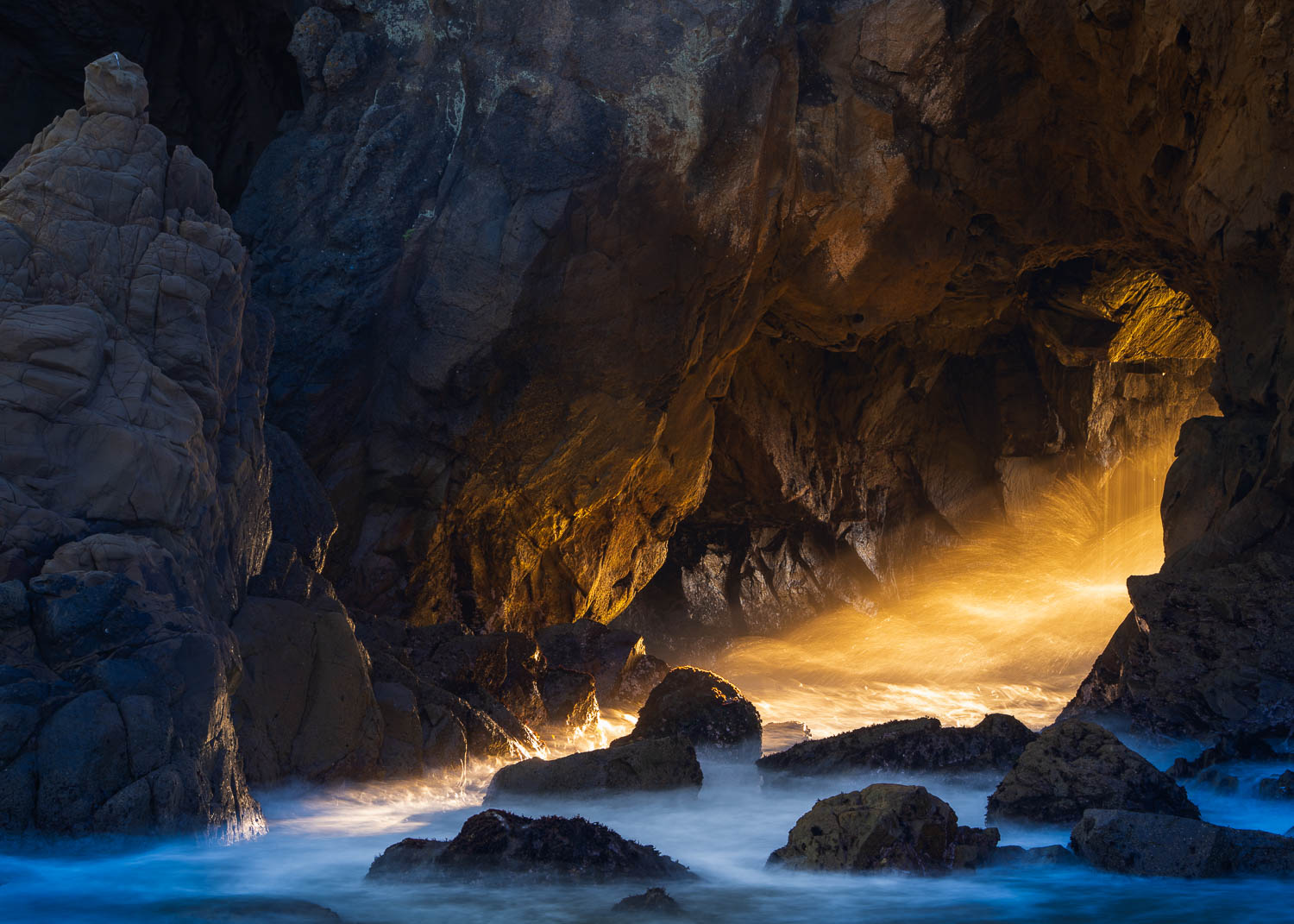 Portal on Fire Beam of golden light through rocky arch and waves crashing